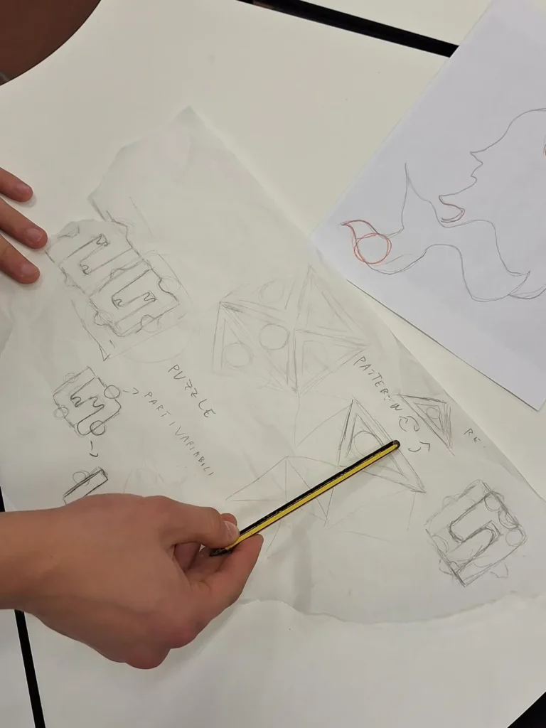 primo piano sulle mani di una studentessa che con l'uso di un foglio di carta trasparente ricalca da una foto della citta, delle forme utili al progetto